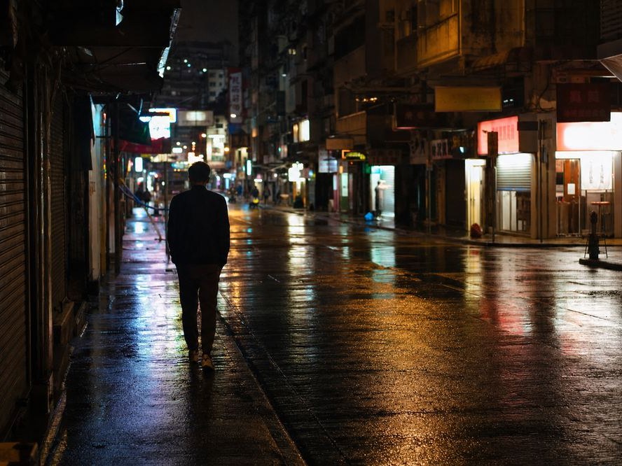 夜晚香港街頭，一個人影喺遠處行緊，濕滑路面反映燈光，象徵低調跟蹤觀察