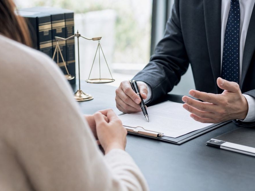 辦公室內律師同客戶隔桌傾談，桌上有天秤擺設同文件夾，象徵尋求法律諮詢嘅場景